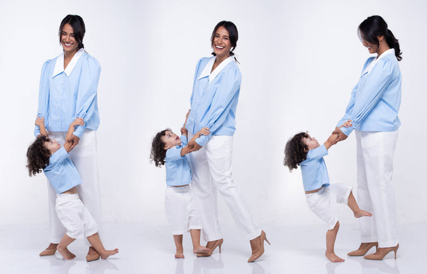 Asian Mother and Caucasian Daughter stand and wear same blue pant dress together. Little girl hold mom hand and smile with love. White background isolated - Фото, зображення