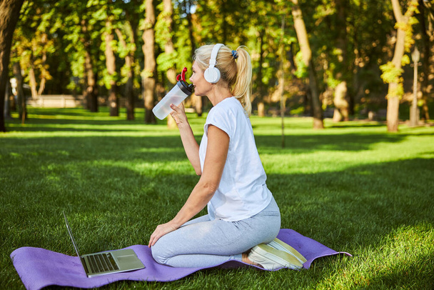 Beautiful woman drinking water and using notebook in park - Foto, imagen
