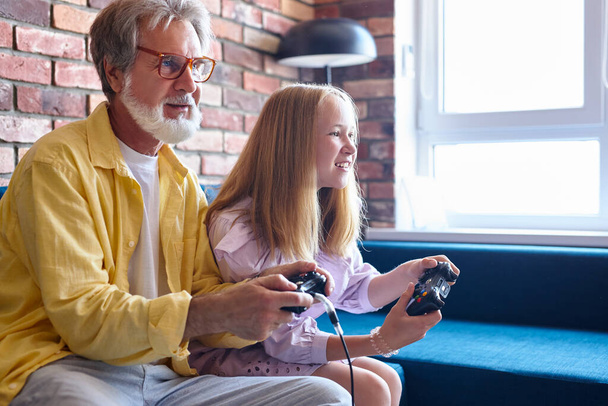 funny grandpa and girl playing video game with console at home - Fotografie, Obrázek
