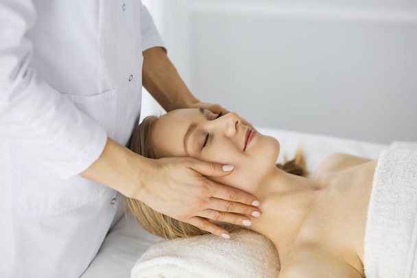 Beautiful caucasian woman enjoying facial massage with closed eyes in spa salon. Relaxing treatment in medicine and Beauty concept - Foto, Imagen