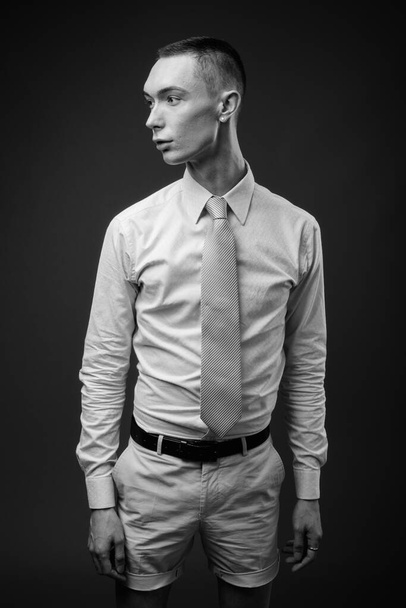 Studio shot of young handsome androgynous businessman against gray background in black and white - Фото, изображение