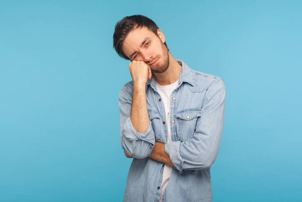 Portrait of unhappy depressed man feeling bored with tedious conversation, looking at camera with disinterest and apathy, indifferent to life, lack of energy. studio shot isolated on blue background  - Foto, imagen
