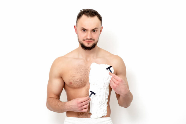Fiatal, szakállas kaukázusi férfi borotvával borotválja a mellkasát fehér borotvahabbal fehér háttéren. Az ember borotválja a törzsét. - Fotó, kép