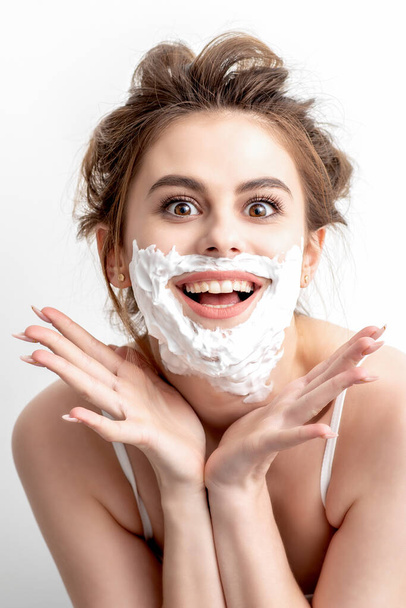 Красивая молодая белая женщина с пеной для бритья на лице позирует на белом фоне - Фото, изображение