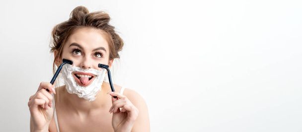 mooie jonge Kaukasische vrouw scheren haar gezicht door twee scheermesjes met tong uit op witte achtergrond. - Foto, afbeelding