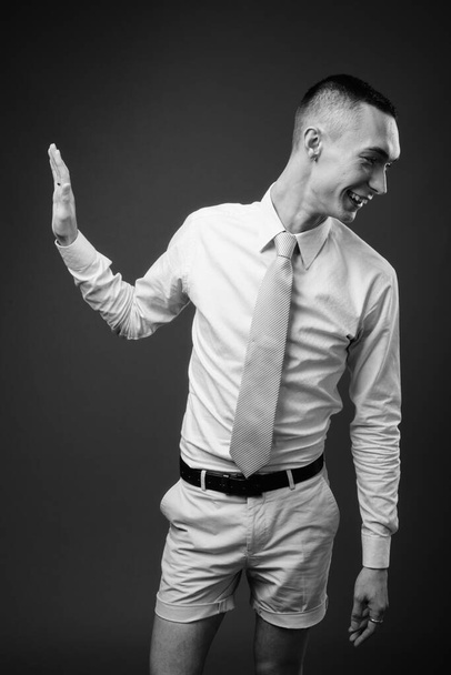 Studio shot of young handsome androgynous businessman against gray background in black and white - Foto, Imagem