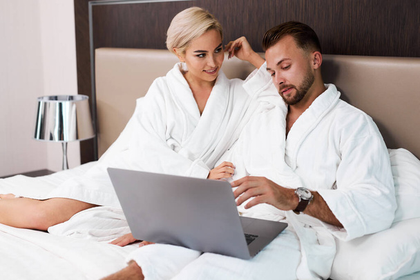 beautiful couple lie on bed with laptop - Фото, изображение