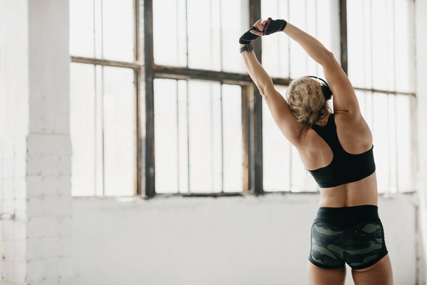 Rozciąganie i motywacja. Muskularna kobieta w odzieży sportowej z nadajnikiem fitness i słuchawkami do ćwiczeń - Zdjęcie, obraz