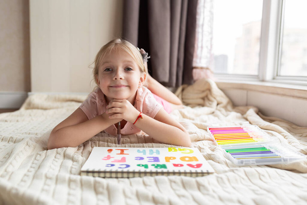 Little child english online at home. Homeschooling and distance education for kids. Girl student drawing english letters at the notebook during coronavirus covid-19 quarantine. High quality photo - Photo, Image
