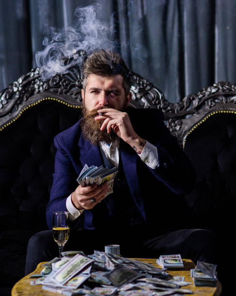 Businessman with beard has cigar, champagne and dollars. - Foto, afbeelding