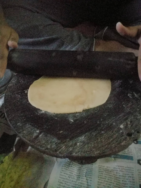 Hacer chapathi utilizando harina de trigo y el uso de tablón y rodillo para hacerlo en forma redonda.El rodillo y el tablón en el que se hace tiene color negro y el uso de forma redonda rodillo se hace. - Foto, Imagen