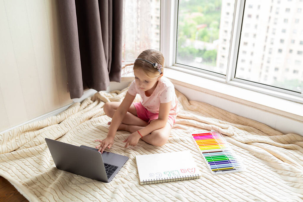 Little child english online at home. Homeschooling and distance education for kids. Girl student drawing english letters at the notebook during coronavirus covid-19 quarantine. High quality photo - Fotografie, Obrázek