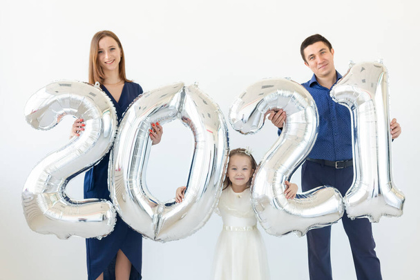 Νεαρή ευτυχισμένη οικογένεια μητέρα και ο πατέρας και η κόρη στέκεται κοντά μπαλόνια σε σχήμα αριθμούς 2021 σε λευκό φόντο. Νέο έτος, Χριστούγεννα, διακοπές - Φωτογραφία, εικόνα