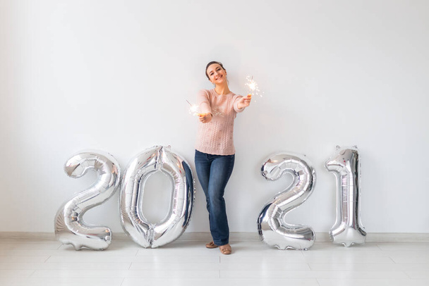 Újévi ünneplés és party koncepció - Boldog fiatal nő csillagszórók közelében ezüst 2021 léggömbök fehér alapon. - Fotó, kép