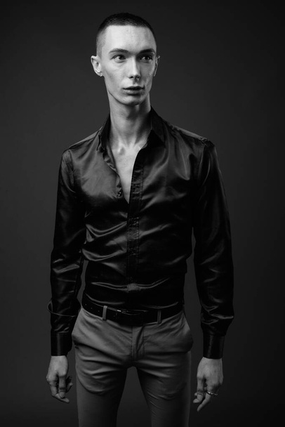 Studioaufnahme eines jungen hübschen androgynen Geschäftsmannes im Seidenhemd vor grauem Hintergrund in schwarz-weiß - Foto, Bild