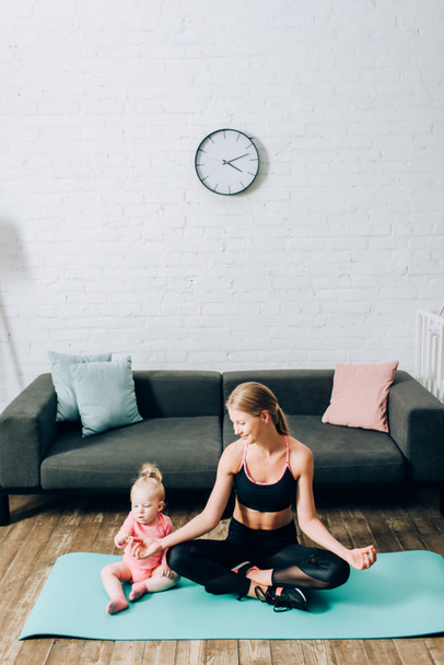 Anya sportruházatban ül jóga pózban közel csecsemő lánya fitness mat - Fotó, kép