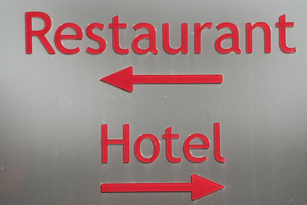 restaurant and hotel sign on a building, red letters on gray sign with direction arrows - Photo, Image