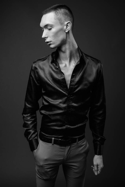 Студийный снимок молодого красивого андрогинного бизнесмена в шелковой рубашке на сером фоне в черно-белом - Фото, изображение