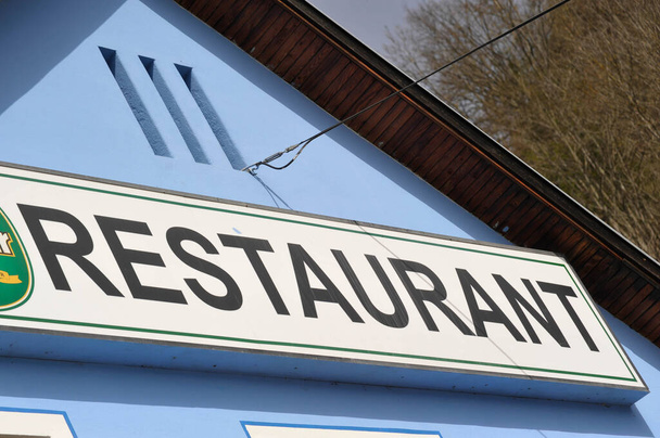 restaurant bord op een gebouw, zwarte letters op wit bord, blauwe huismuur - Foto, afbeelding