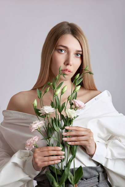 Beauty portrait  woman with pink eustoma flowers in her hands. Natural cosmetics for face and body skin care. Beautiful girl in a white shirt - Foto, Imagen