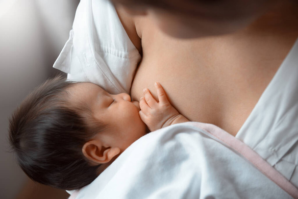 Close-up young woman breastfeeding her baby on blurred background. - 写真・画像