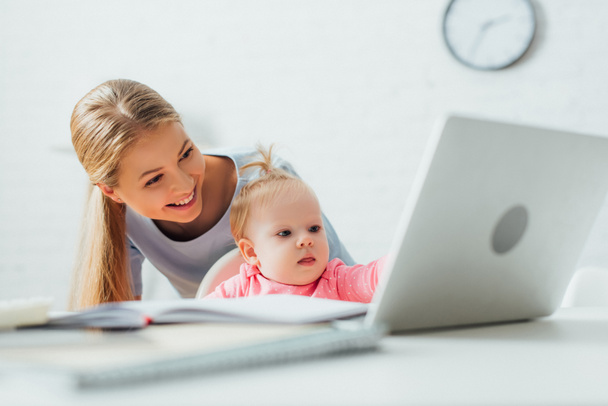 Enfoque selectivo de la madre de pie cerca del niño mirando el ordenador portátil y artículos de papelería en la mesa  - Foto, Imagen