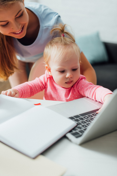 Selective focus of infant touching laptop near mother at home  - Fotó, kép