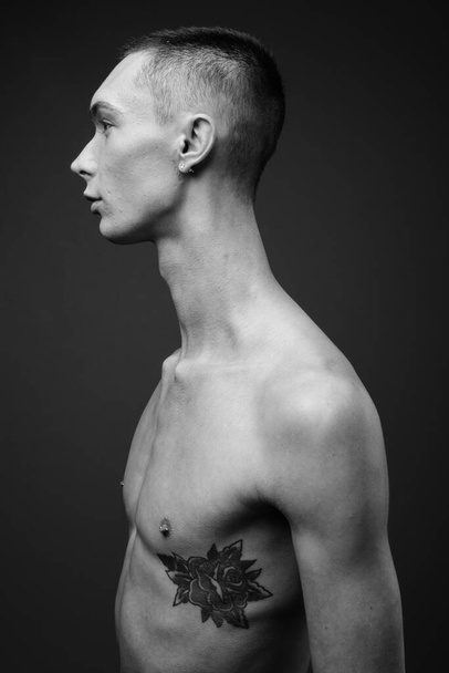 Estudio plano de joven guapo andrógino hombre sin camisa sobre fondo gris en blanco y negro - Foto, imagen