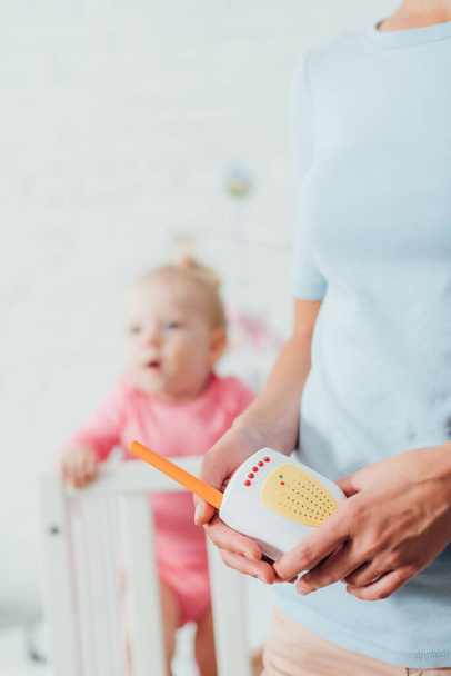 Selective focus of woman holding baby monitor near daughter at home  - Photo, Image