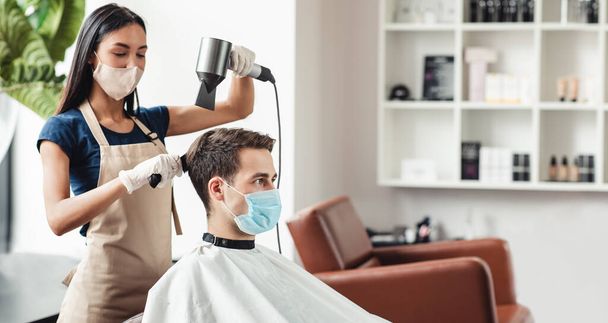 Parrucchiere e cliente in salone in maschere mediche durante la pandemia virale - Foto, immagini