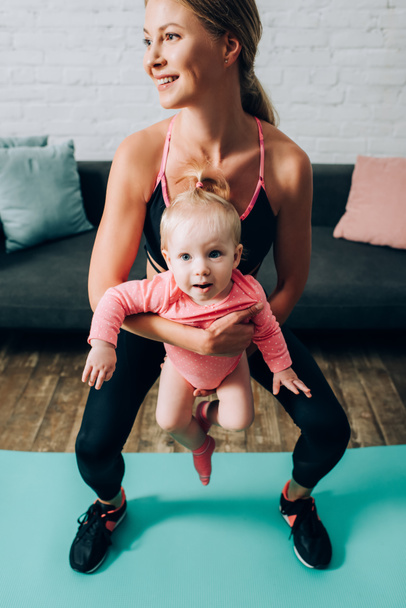 Anya sportruházatban tartja baba lány edzés közben fitness mat otthon  - Fotó, kép