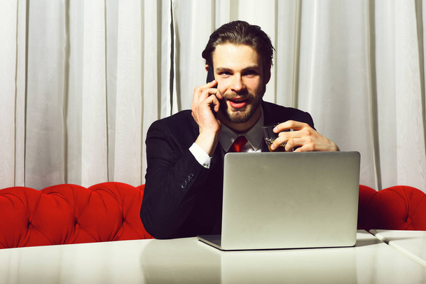 bearded man, businessman holding glass of whiskey works at laptop - Zdjęcie, obraz