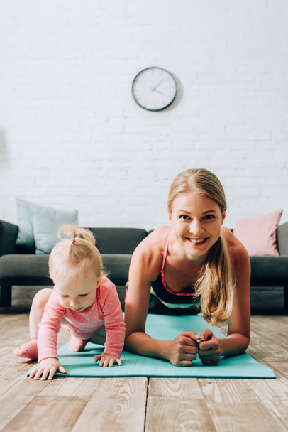 Selective focus of sportswoman doing plank near baby girl on fitness mat  - Photo, Image