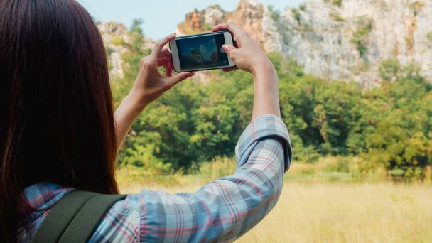 Veselý mladý cestovatel asijské dáma s batohem pomocí smartphone pro focení na horském jezeře. Korejská dívka si užívat dovolenou dobrodružství pocit šťastné svobody. Životní styl cestování a relaxace koncept. - Fotografie, Obrázek