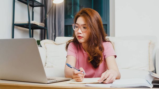 Юная азиатская студентка-подросток дистанционно учится у онлайн-учителя и учится на компьютере в гостиной из дома по ночам. Социальное дистанцирование, карантин для предотвращения коронных вирусов. - Фото, изображение