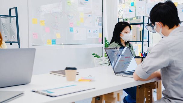 Asia businesspeople entrepreneur wearing medical face mask for social distancing in new normal situation for virus prevention while using laptop back at work in office. Lifestyle after corona virus. - Foto, imagen