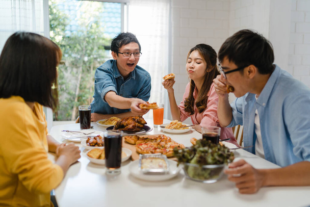 Szczęśliwa grupa młodych przyjaciół je lunch w domu. Azjatycka impreza rodzinna jedząca pizzę i śmiejąca się z posiłku siedząc razem przy stole w domu. Święto i wspólne świętowanie. - Zdjęcie, obraz