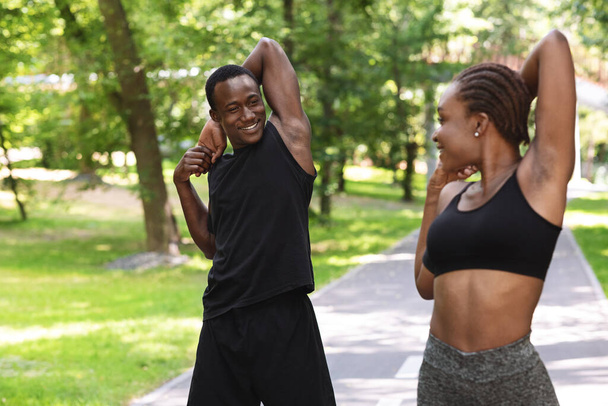 Young african couple doing sports outdoors, exercises in summer park, stretching muscles - Φωτογραφία, εικόνα