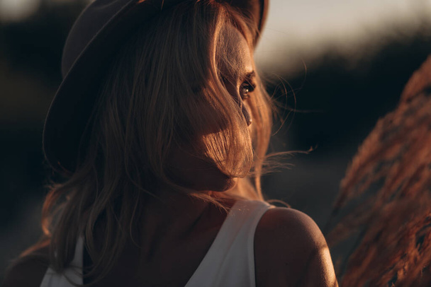 Красивая блондинка в шляпе и белом платье в джинсовой куртке ходит по пустынной дороге - Фото, изображение