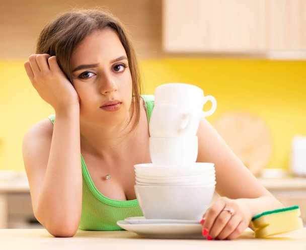 Молодая женщина моет и моет посуду на кухне - Фото, изображение