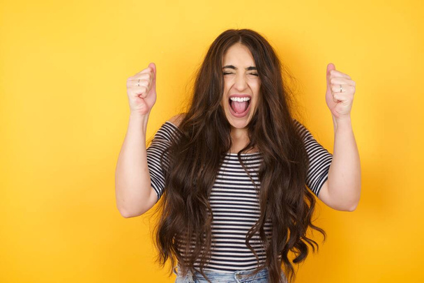 Caucasian brunette woman rejoicing her success and victory clenching her fists with joy. Lucky woman being happy to achieve her aim and goals. Positive emotions, feelings. - Photo, Image