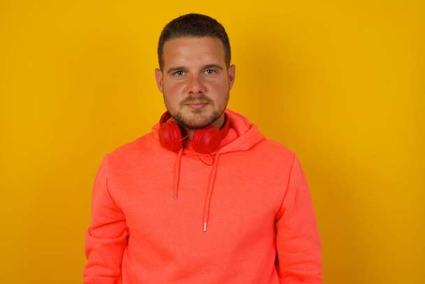 Junger schöner Mann mit Kopfhörern gegen gelbe Wand  - Foto, Bild