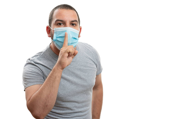 Aikuinen mies tekee olla hiljaa ele käyttäen etusormi suun yli yllään kertakäyttöisiä covid19 sars influenssa pandemia naamio tyhjä copyspace eristetty valkoisella pohjalla - Valokuva, kuva