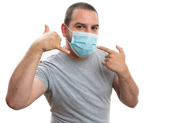 Male adult pointing index finger at disposable medical or surgical protection mask making call gesture using hand as phone isolated on white studio background - Photo, image