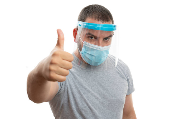 Tek kullanımlık cerrahi ya da medikal giyimli erkek modeli. Grip önleyici 19 grip maskesi. Baş parmağının beyaz stüdyo arka planında izole edilmiş bir jest olduğunu gösteriyor. - Fotoğraf, Görsel