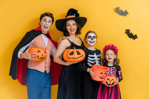 Mother, father and their kids having fun at party. Happy family celebrating Halloween. People wearing carnival costumes and makeup on yellow wall background. - Fotografie, Obrázek