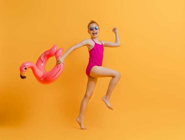 Happy child wearing swimsuit. Girl with swimming ring flamingo. Kid on a colored yellow background. - Photo, Image