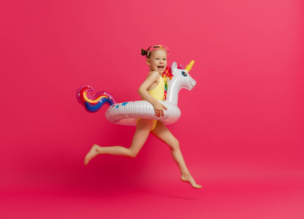 Happy child wearing swimsuit. Girl with swimming ring flamingo. Kid on a colored pink background. - Фото, изображение