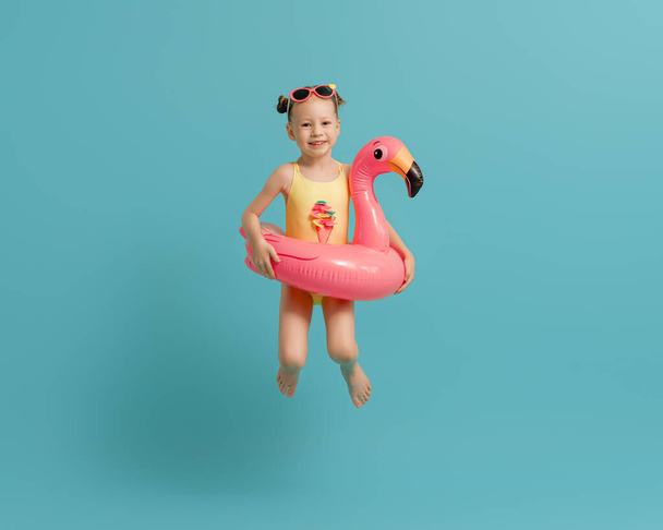 Happy child wearing swimsuit. Girl with swimming ring flamingo. Kid on a colored turquoise background. - Foto, Imagem