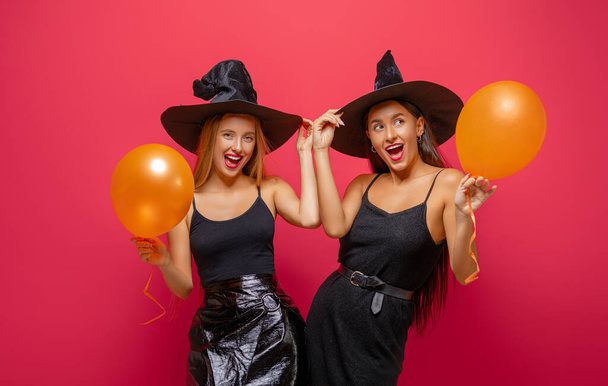 Happy Halloween! Two young women in black witch costumes on party on red color background. - Fotografie, Obrázek